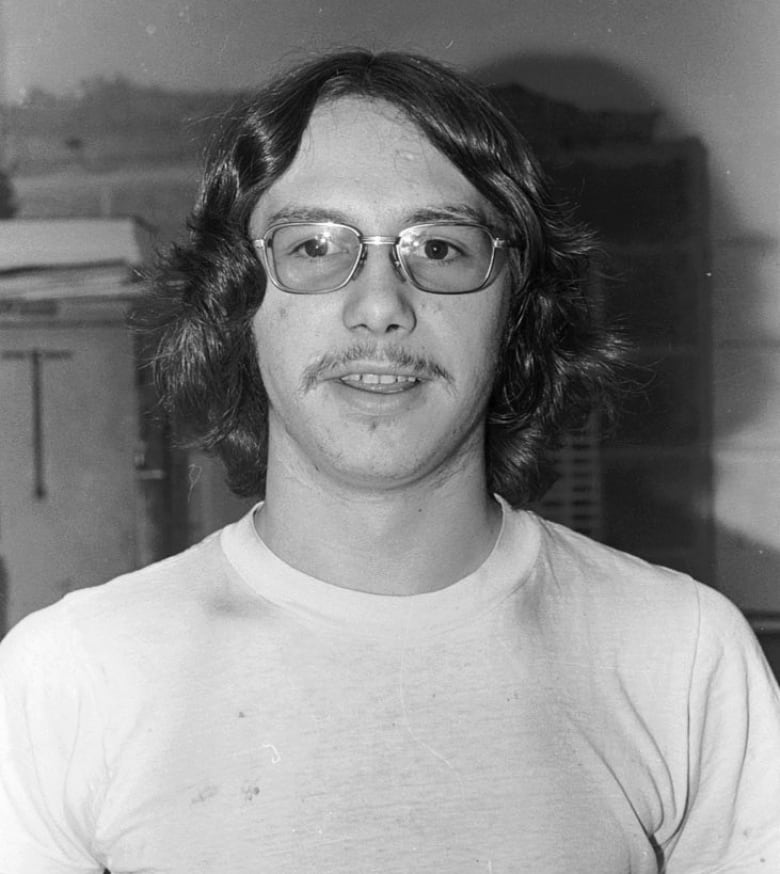 A black and white portrait of a man in glasses with long hair and a mustache. 