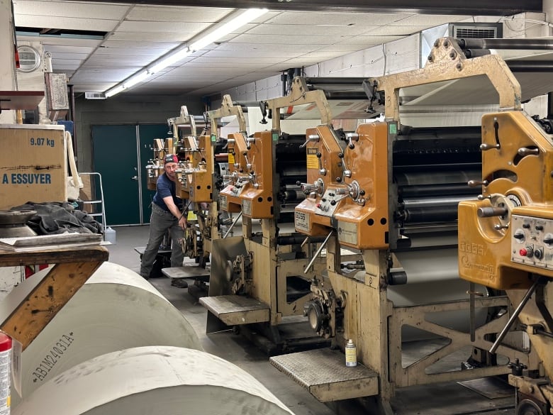 A man stands with his hand on a lever at the end of a row of machines.