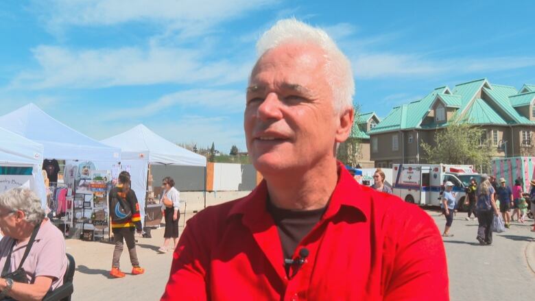 A man wearing red smiles in an outdoor setting. The weather is summer-like. 