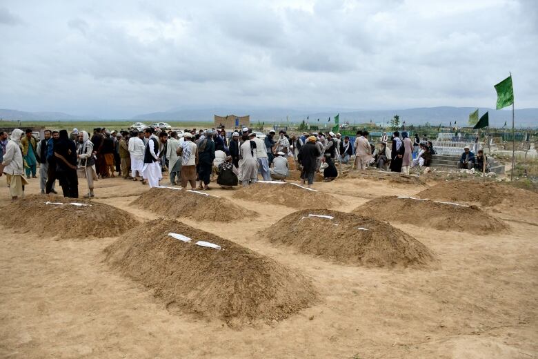 People gather around mounds of dirt in a burial site