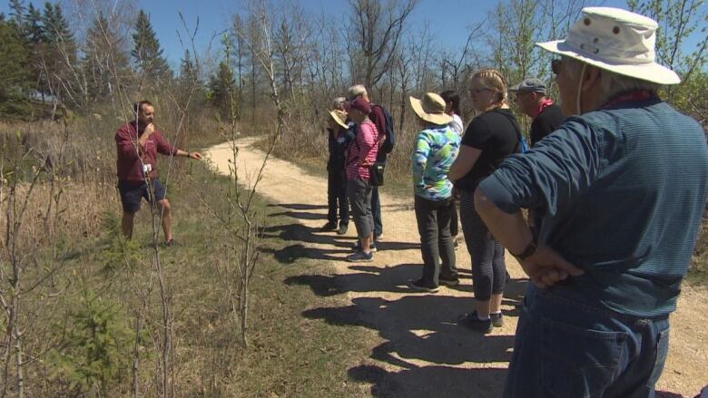 People stand on an outdoor trail, listening to a man.