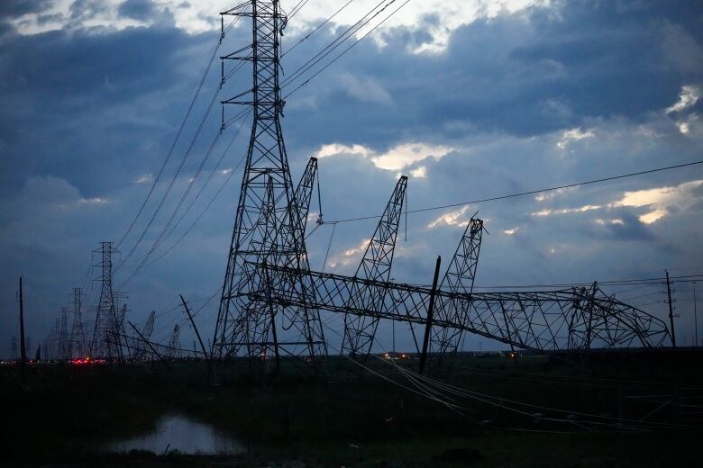 A transmission tower lies on its side next to a row of still-standing towers that stretches into the distance.