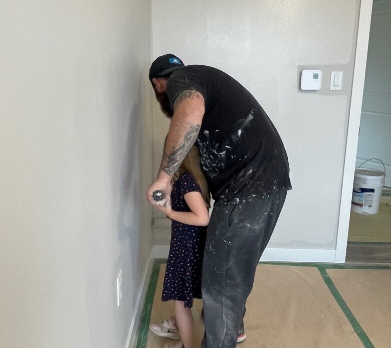 A man and girl with backs to camera paint the wall in a house grey.