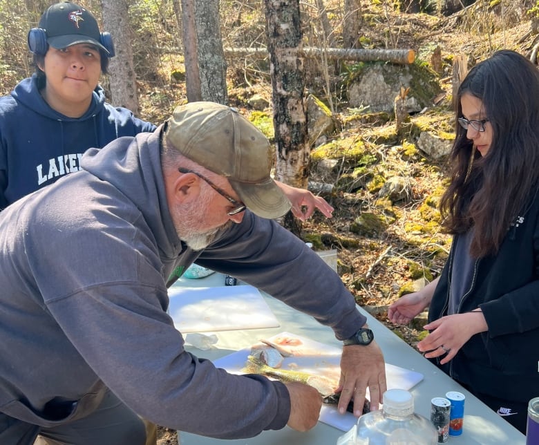 a man is filleting a fish on the shore as the students learn and then try it for themselves.