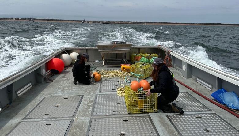 Two women move fishing traps on the back of a boat.