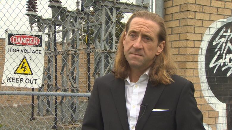 Man with shoulder length brown hair, frowning.