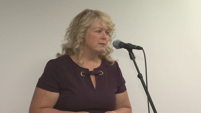 A woman in a coffee-coloured top speaks into a microphone.