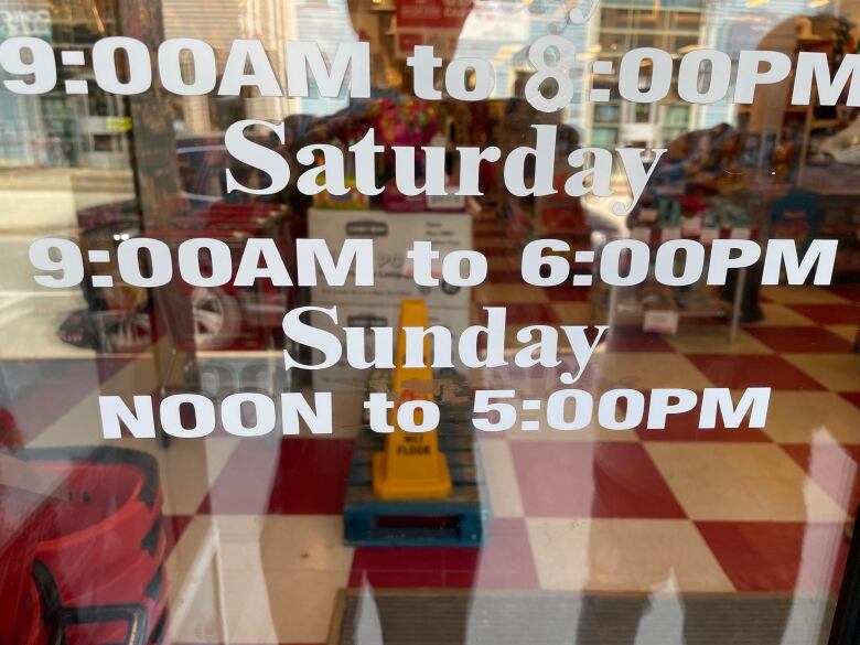 Hours on door window showing it is open from noon to 5 p.m. on Sunday