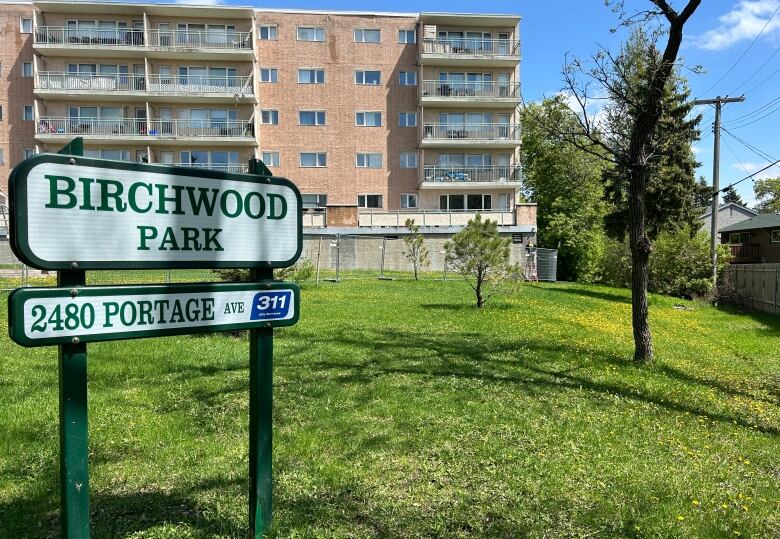 A sign in a greenspace that says Birchwood Park is shown in front of a five-storey apartment building.