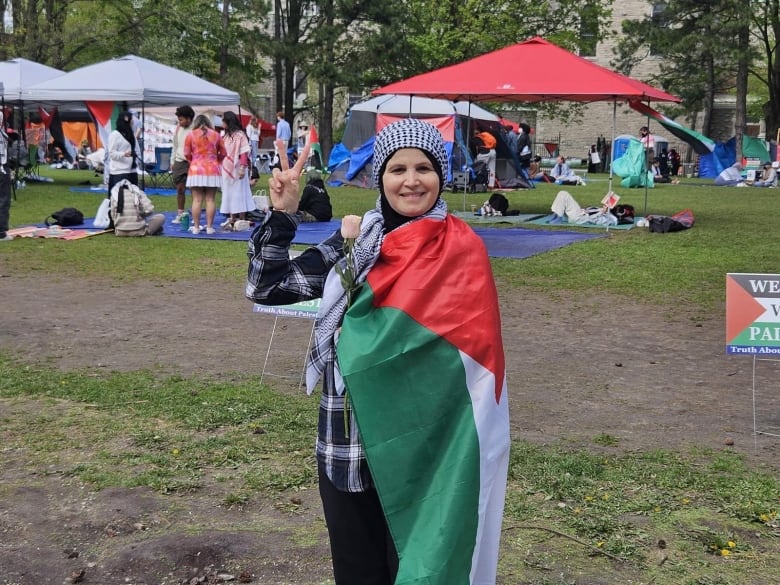 A woman with a Palestinian flag around her shoulders putting up a peace symbol.