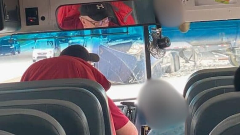 View from the back of a school bus. A driver sits next to a student. Outside the window is debris from a crash.