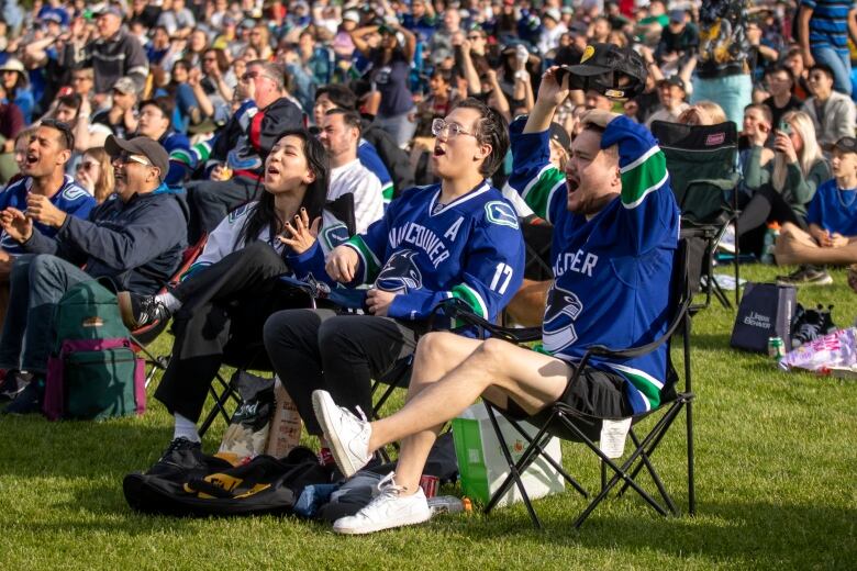 Fans wearing blue gesture in surprise and shock at a large outdoor event in a park.