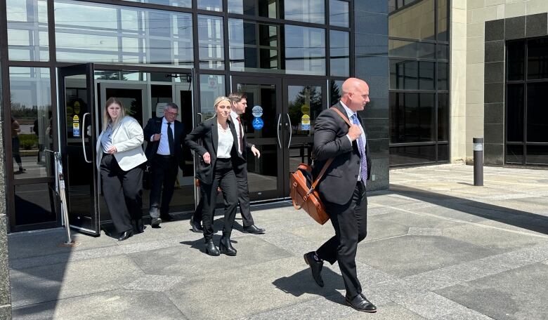 A man with a brown bag walking out of a set of doors with others following behind.