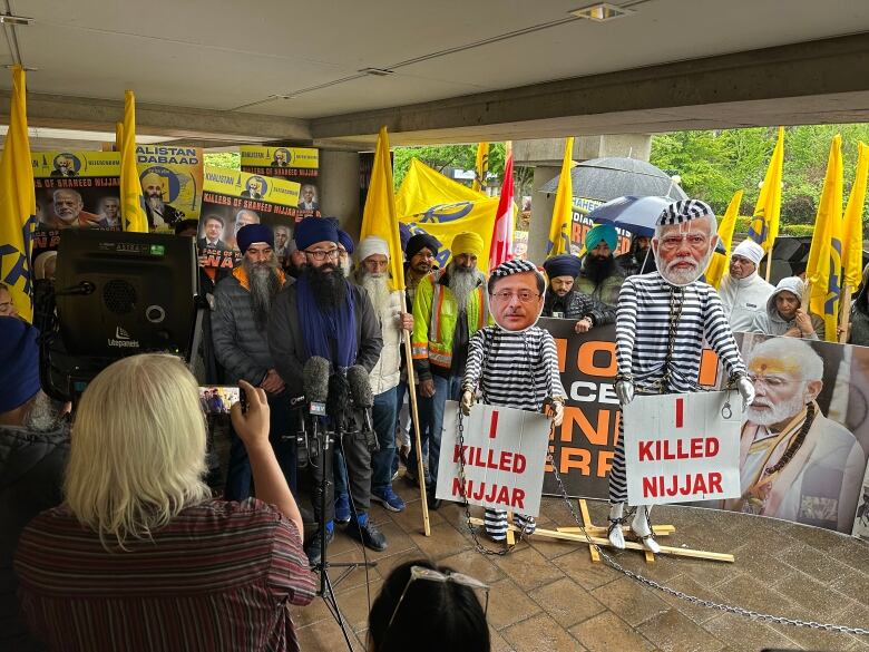 A protest outside a court house with pictures of two men on puppets with handcuffs and prison suits with signs that say 'I killed Nijjar.'