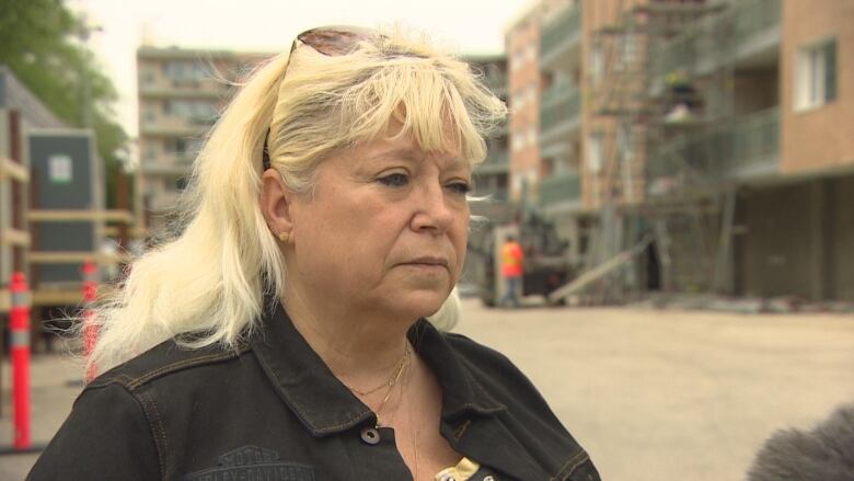 A woman is pictured looking forward. A building under construction is behind her.