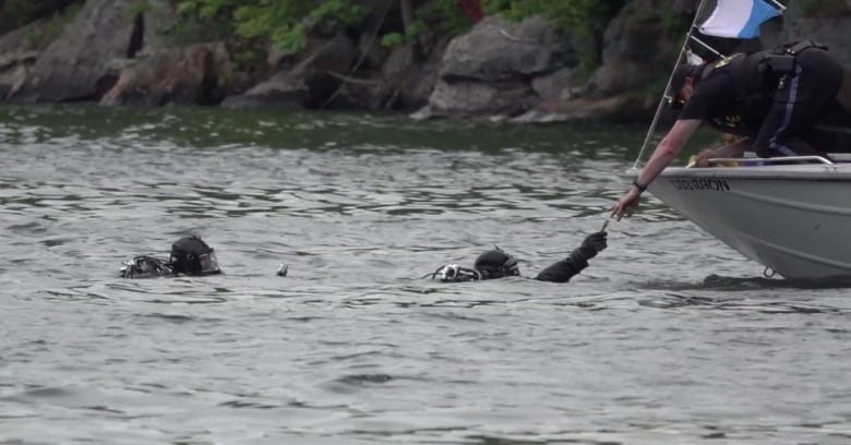 Police divers hand over an object to police on a boat.