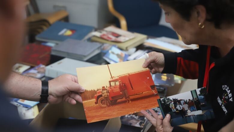 Two people hold a photo of two men standing in front of an old fire truck.