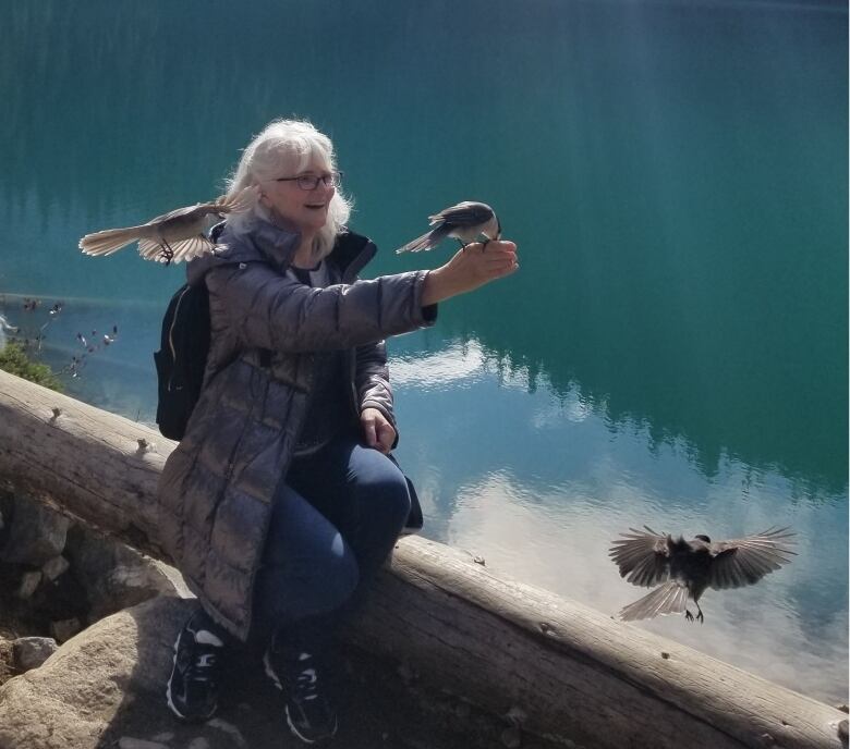 A senior woman with several birds outdoors.