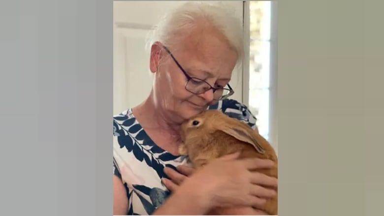 A senior woman cradles a live rabbit.