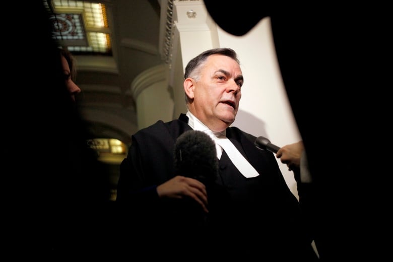 A white man wearing a speaker's uniform speaks to reporters.