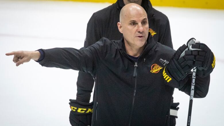 A bald white man wearing hockey gear points to his right while on the ice.