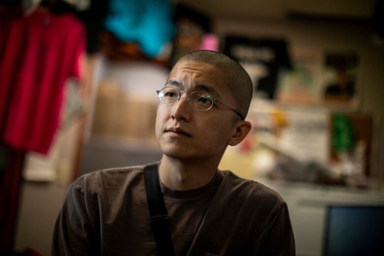 A man with a shaved head in glasses and a brown shirt.