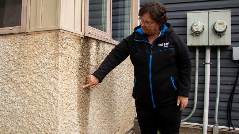 A woman points to water damage on the side of a building.