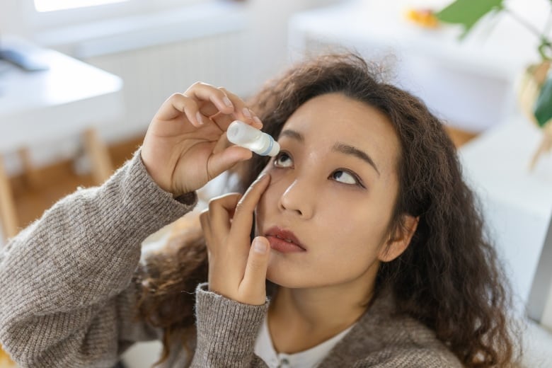 A woman puts an eye drop in her eye.