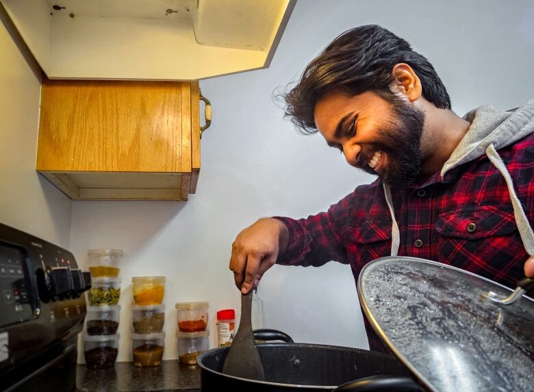 A smiling, bearded dark-haired stirs something cooking in a pot.