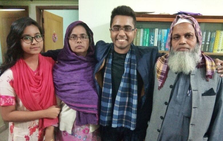 Four people stand for a family picture, their arms around each other.