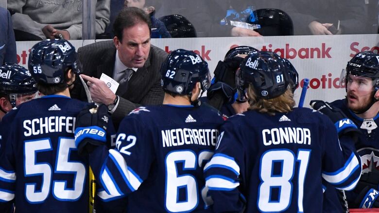 A man in a suit speaks with three hockey players.