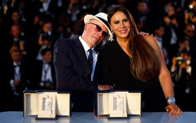 Two people embrace as awards are displayed on a table.