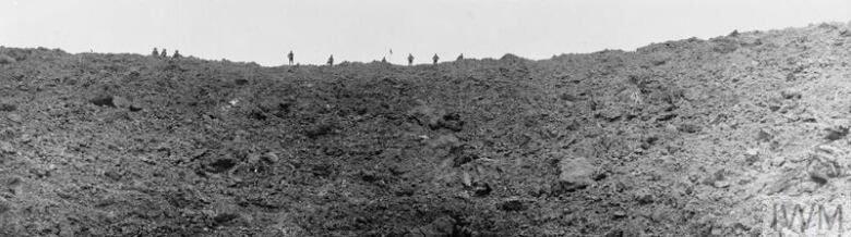 Soldiers in uniform stand at the rim of a deep crater in the earth.