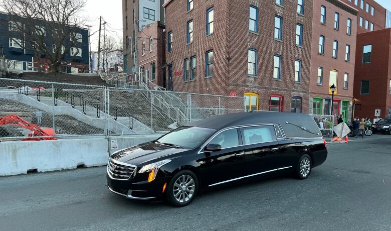 A black hearse drives by a construction site.