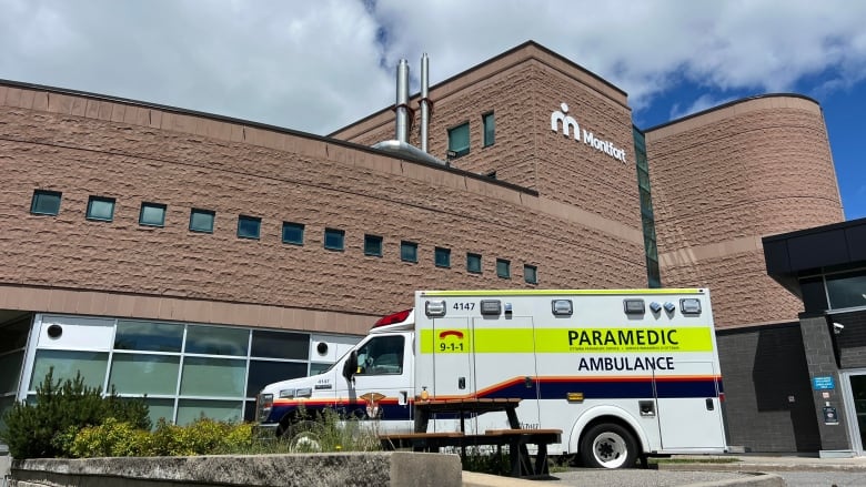 The outside of a hospital with an ambulance parked nearby. 