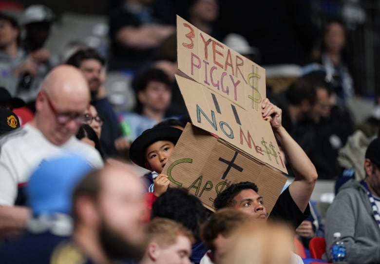 A fan holds up a sign reading '3 Year Piggy $' and 'No Messi'.