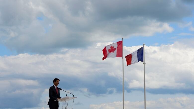 A man stands at a podium with the Canadian and French flags behind him.