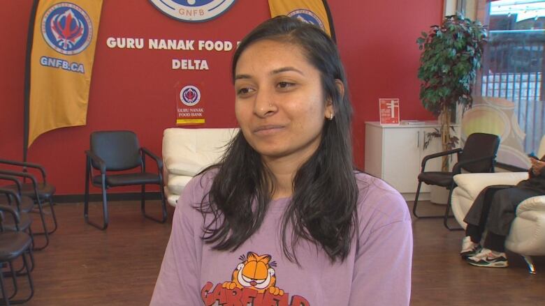 A woman in a purple shirt stands in front of some chairs at the Guru Nanank Food Bank.