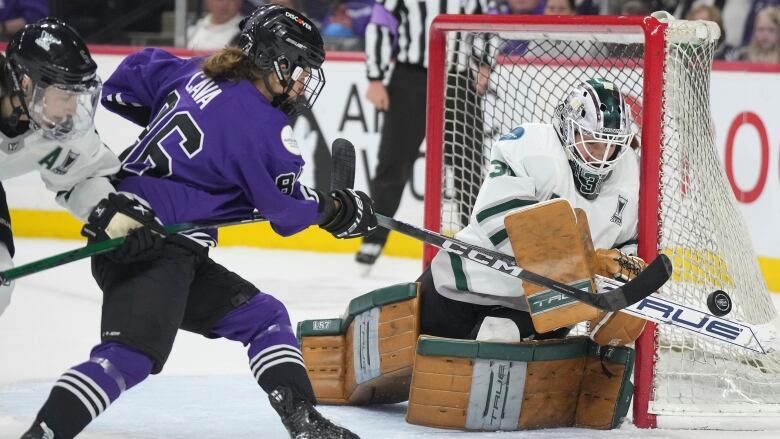 A female ice hockey player shoots on a goaltender from close range during a game.