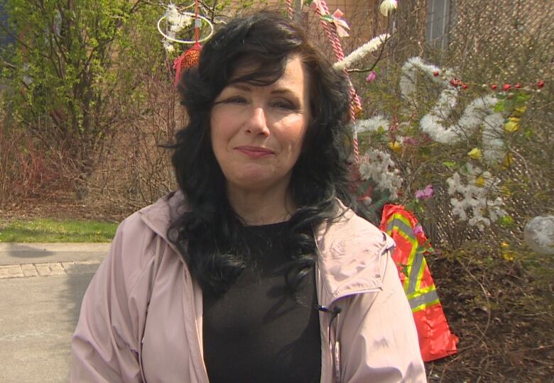 Woman with long brown hair, wearing black shirt and pink jacket.