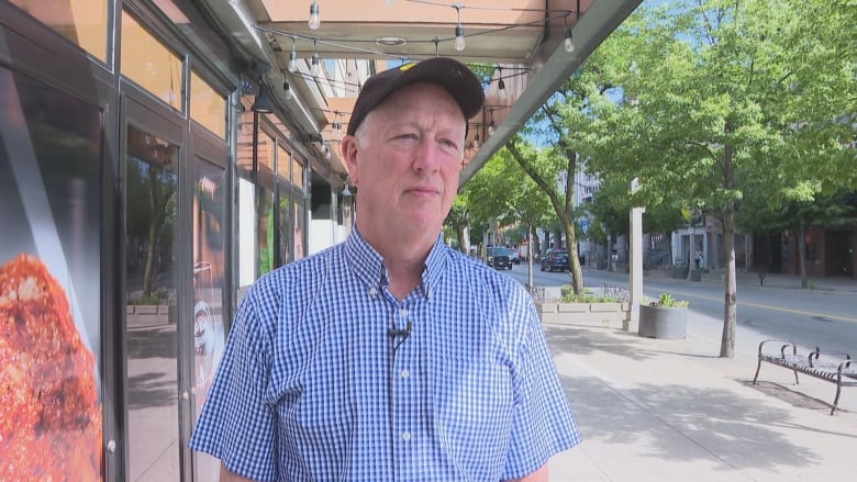 A man stands on the street and looks off-camera.