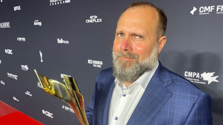 A man stands on a red carpet holding a trophy.