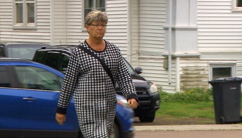 A woman walks past the camera with a black and white dress on. She has short hair and a blank face. 