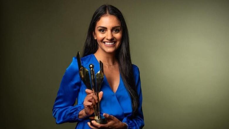 A woman wearing a blue dress holds an award