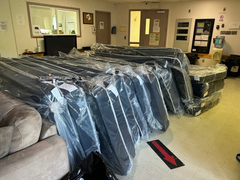 Dozens of mattresses wrapped in plastic stored in a room. 