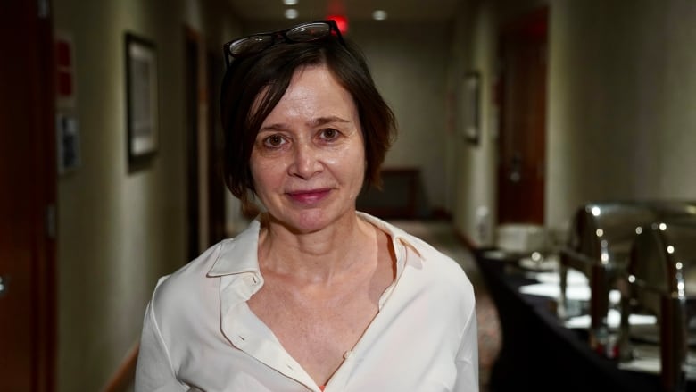 A woman stands in a hallway looking at the camera.