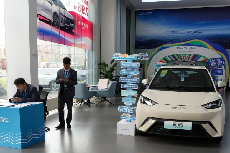 Sales staff stand near the Seagull electric vehicle from Chinese automaker BYD at a showroom in Beijing, Wednesday, April 10, 2024. The tiny, low-priced electric vehicle called the Seagull has American automakers and politicians trembling. The car, launched last year by Chinese automaker BYD, sells for around $12,000 in China. But it drives well and is put together with craftsmanship that rivals U.S.-made electric vehicles that cost three times as much. Tariffs on imported Chinese vehicles probably will keep the Seagull away from Americas shores for now.