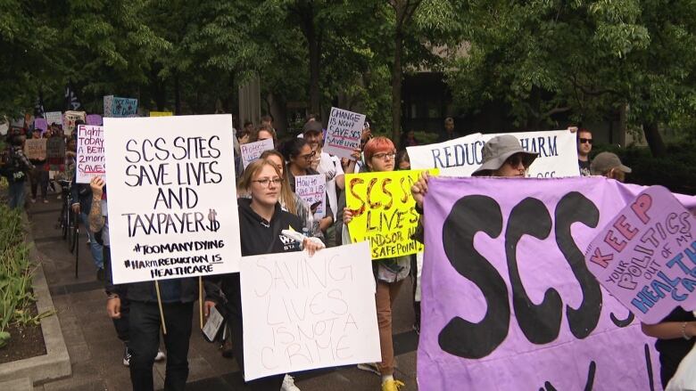 A rally marched holding signs in support of supervised drug consumption sites. One reads: Saving lives is not a crime.