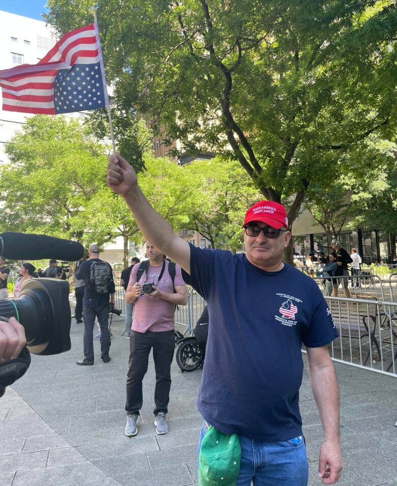 Man waving upside-down US flag, wearing red MAGA cap