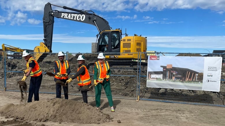 Four people toss shovels of dirt to break the ground on the construction of a new fire station.